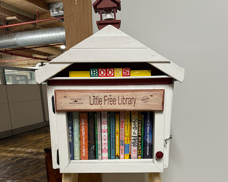 an image of the first Little Free Library box, a white wooden structure with a glass door that holds books inside on a shelf